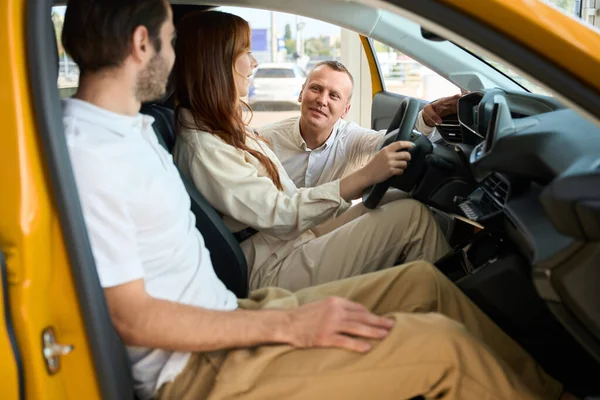 汽车销售顾问与坐在新车上的妇女和她的伴侣交流 — 图库照片