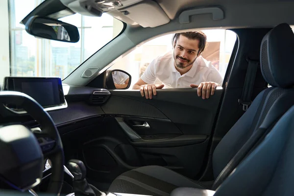stock image Smiling pleased young potential buyer looking at automotive upholstery through open window