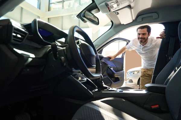 Joyous Caucasian automotive dealership client looking inside passenger car through open door
