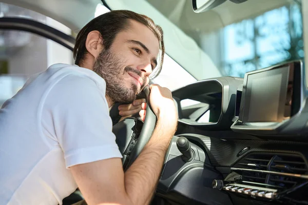 Uśmiechnięty Młody Człowiek Siedzi Samochodzie Przytula Się Kierownicy Samochodu — Zdjęcie stockowe