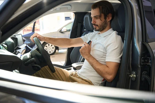 Calm focused buyer with key fob in hand sitting behind steering wheel of automobile