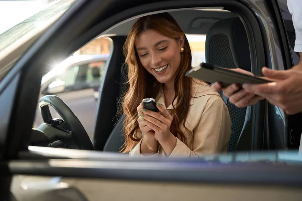 Joyous automobile dealership customer inspecting auto key fob in presence of sales consultant