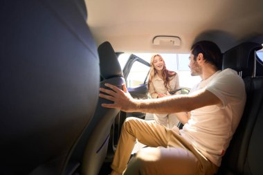 Motorlu taşıt içinde oturan adam neşeli genç oto galerisi satıcısıyla konuşuyor.