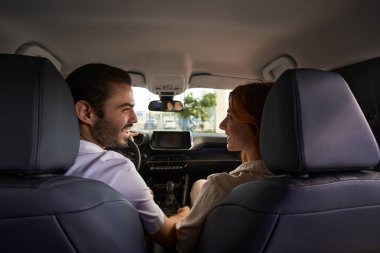 Neşeli adam direksiyonda oturmuş neşeli bayan arkadaşına bakıyor.