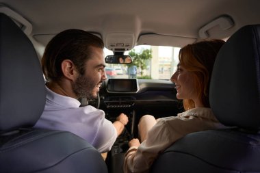 Neşeli genç sürücü direksiyonda oturuyor ve araba yolcularına gülümsüyor.