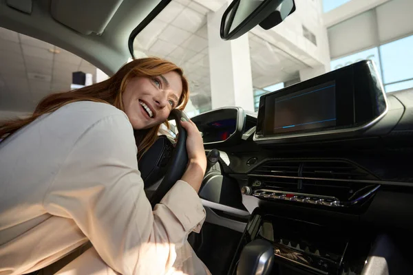 Smiling happy auto dealership customer lying on steering wheel of luxury car