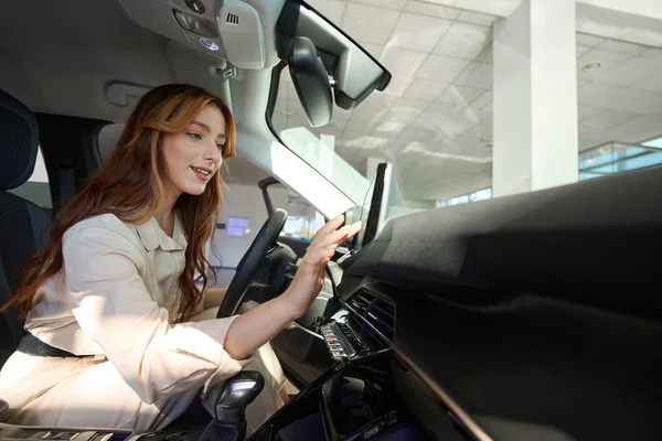 Smiling young woman seated in driver seat tapping on vehicle on-board computer