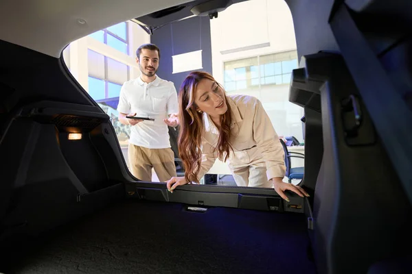 Auto dealership client looking at open car trunk in presence of sales consultant