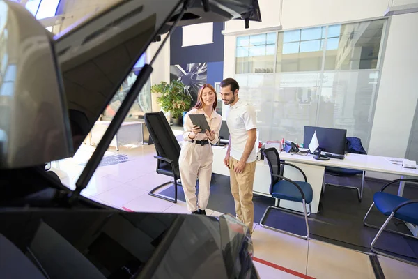 Smiling car salesperson demonstrating information on tablet touch screen to potential buyer