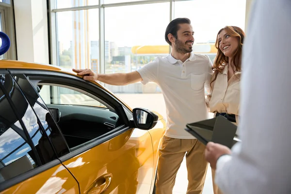 高級車の横に立つ喜びの男性と笑顔で幸せな女性コンパニオンで営業マンの前で — ストック写真