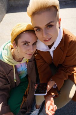 Sarışın ve esmer, taş merdivenlerin arka planında selfie çekiyorlar. Büyük bir şehirde yaşayan lgbt çifti.