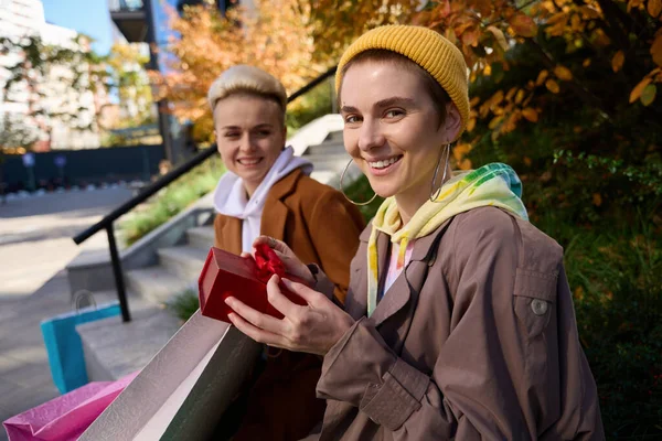 Радостная Женщина Держит Красную Коробку Подарком Руках Подруга Сидит Рядом — стоковое фото