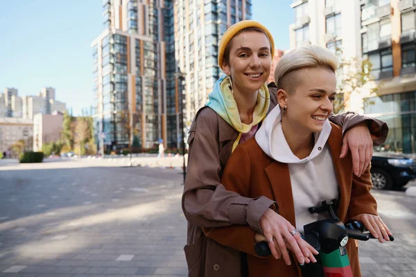 陽気な若い女性 Lbtカップル カジュアルな服で 秋の晴れた日に大都市のスクーターに一緒に乗る — ストック写真