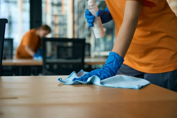 stock image Two cleaning women disinfect tables in the coworking area with special products, they are wearing protective rubber gloves