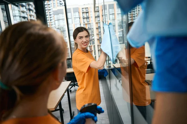 職場の窓を掃除する清掃会社の若い女性従業員 彼らは良い気分で働いています — ストック写真