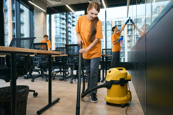 Female cleaning company team in overalls cleans and disinfects the coworking space, they use a vacuum cleaner and wipes