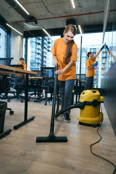 Energetic cleaning company team in uniform washes and disinfects the coworking space, they use a vacuum cleaner, scraper and wipes