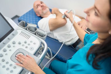 Doktor kolunun üzerinden sensörü geçirirken ciddi bir adam kolunu dirseğinden büktü.