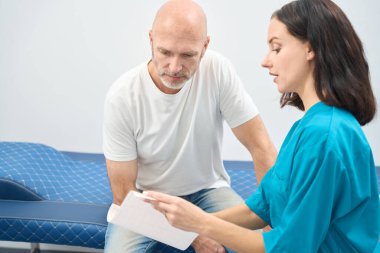 Hevesli bir kadın tıp üniformalı bir adama danışırken o da ellerindeki çıktıya dikkatlice bakıyor.