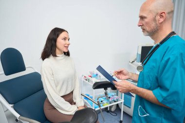 Odaklanmış sağlık çalışanı hastasına tavsiye verirken kendisi de onun karşısında sandalyede oturuyor.