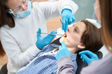 Çocuğa diş çekilmeden önce anestezi, üniformalı bir doktor ve eldiven giyen bir asistan verilir.