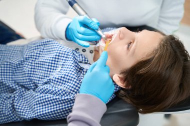 Oğlan tıp fakültesinde diş tedavisi görüyor, doktor işinde bir endomotor kullanıyor.