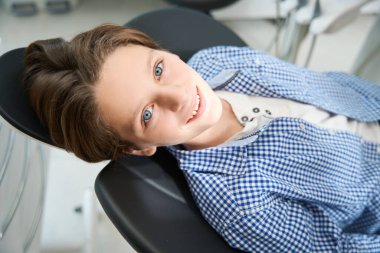 Yakışıklı, gülümseyen genç bir çocuk dişçi koltuğunda oturuyor. Bir uzmanla görüşmeyi bekliyor.