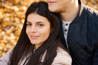 Arkadaşının kollarında büyüleyici genç bir kadın, sonbahar parkında dinlenen bir çift.