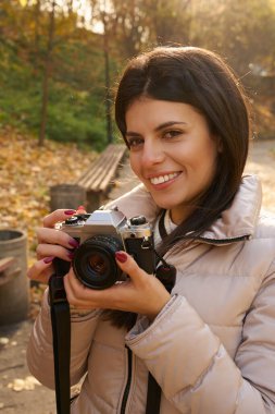 Elinde kamerayla güzel bir genç kadının fotoğrafı. Sonbahar parkında.