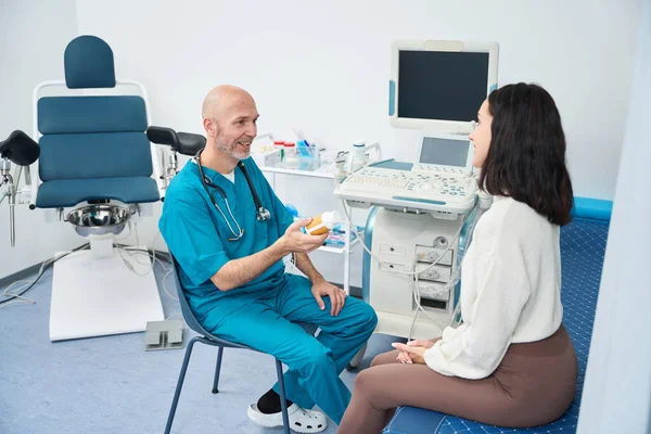 一位快乐的妇科医生坐在一位妇女面前 听着他手里拿着的药丸 — 图库照片