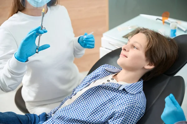 微笑着看着手里拿着麻醉注射器的青少年牙医 穿着制服和手套的女人 — 图库照片