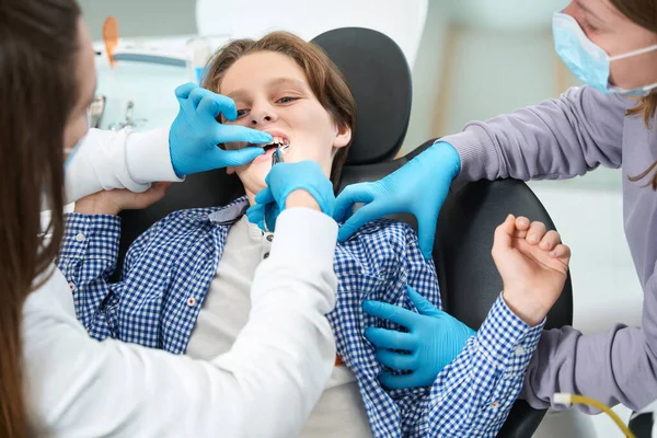 Женщина Дантист Удаляет Зуб Молодому Пациенту Специальным Инструментом Помощник Помогает — стоковое фото