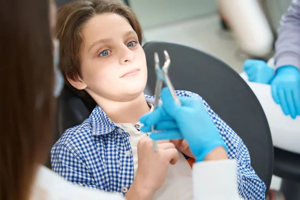 医生在牙医的椅子上吓到了一个年轻的病人 准备了一个拔牙的工具 — 图库照片