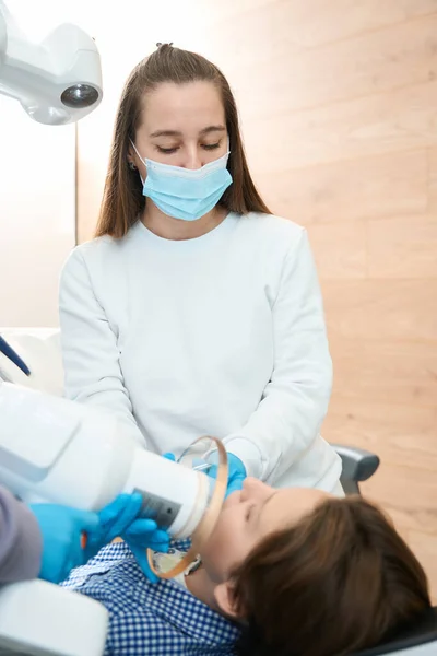 女医生对一名青少年进行了一次牙齿X光检查 她身穿医疗制服 戴着面具和手套 — 图库照片