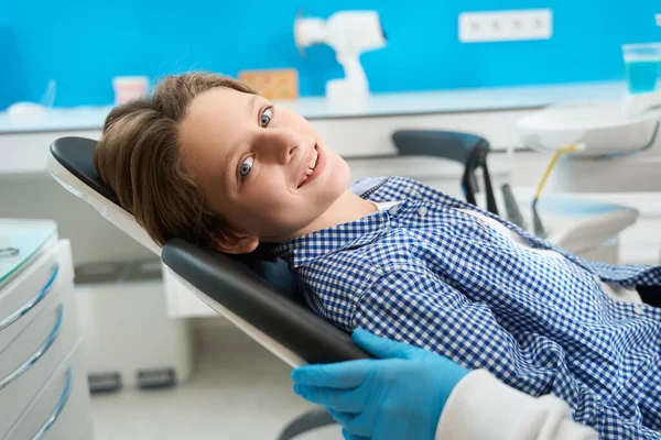 笑着的少年坐在特殊设备中的牙科椅子上 等待一位专家的咨询 — 图库照片