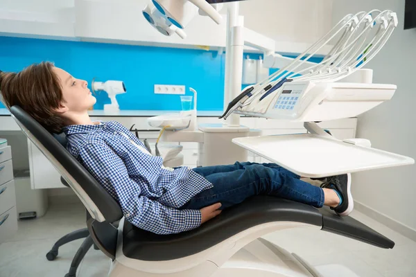 Skoncentrowany Chłopiec Koszuli Kratę Siedzi Spokojnie Krześle Dentystycznym Specjalny Sprzęt — Zdjęcie stockowe