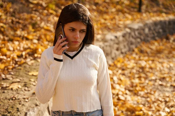 Грустная Молодая Женщина Разговаривает Телефону Против Осенней Листвы — стоковое фото
