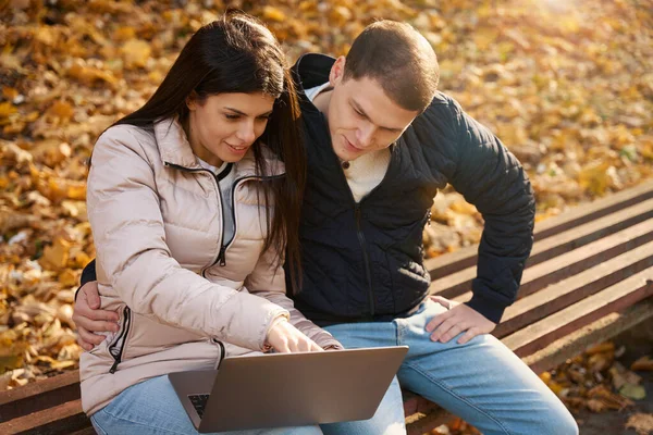 満足した男は彼のガールフレンドの腰の周りに彼の腕を置きます 彼らは一緒にノートパソコンのモニターを見ます — ストック写真