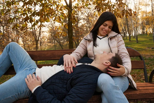 这对可爱的夫妇坐在公园的长椅上 男人把头靠在女友的膝上 看着她的眼睛 — 图库照片