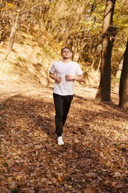 Genç sporcu meşe yolu boyunca koşar, güneşli bir sabahtan hoşlanır.