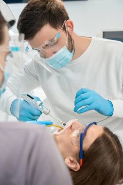 Tek kullanımlık nitril eldivenli doktor, müşteriye diş şırıngası ile anestezi yapıyor.