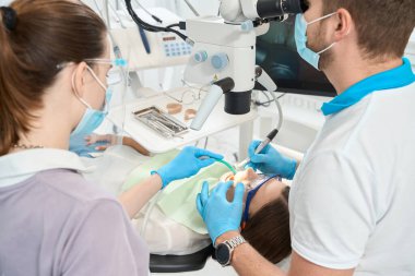 Deneyimli bir diş hijyenisti, hemşire tarafından desteklenen kadın hastada merkezi kesici dişler arasındaki kalkülüsü çıkarıyor.