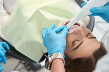 Tek kullanımlık nitril eldivenlerle dişçilerin yakın çekimleri hastanın ön dişlerini teşhis cihazıyla tarıyor.