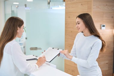 Müşteri, güler yüzlü genç tıbbi resepsiyonistin rıza formunu dolduruyor.