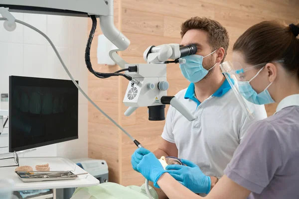 专业牙医在有经验的女护士的协助下 用显微镜治疗病人的牙齿 — 图库照片