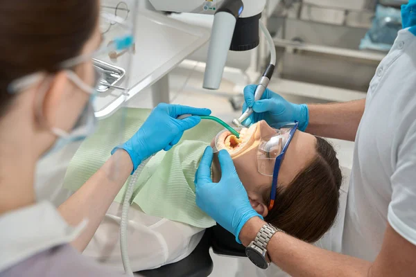 看護師の補助を受けた若い女性の前歯の間のタルタルを除去する組織学者 — ストック写真