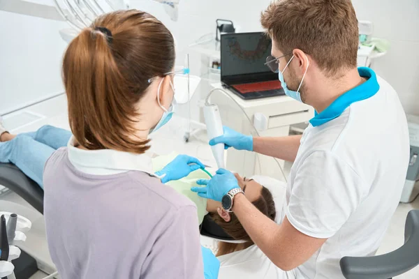 使用现代诊断装置在女护士的协助下对病人口腔进行合格检查的口腔科医生 — 图库照片