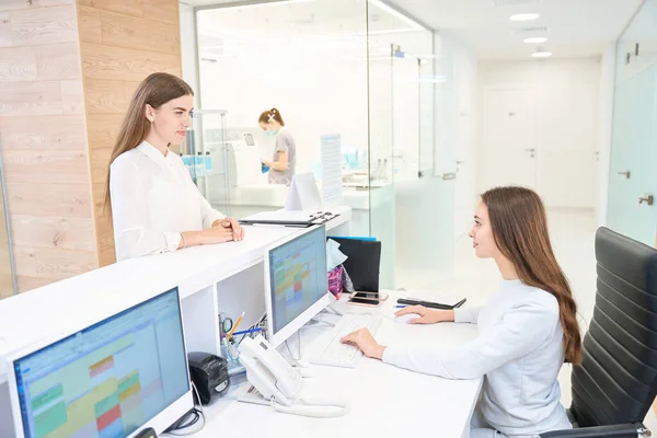 Young Patient Leaning Reception Desk Looking Medical Receptionist Working Desktop — Stock Photo, Image