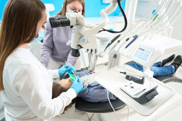 在现代牙科诊所有一名助手的医生正在显微镜下治疗一个男孩 他们使用的是现代设备 — 图库照片