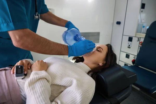 当一名医护人员给她提供氧气并监测她的脉搏时 一个不知情的女人躺在救护车上 — 图库照片